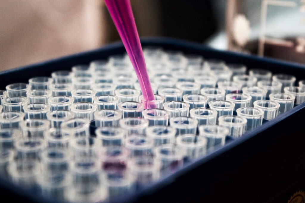 Dropper putting magenta colored fluid in test-tubes for control samples. Best Laboratory Practices for Quality Research.