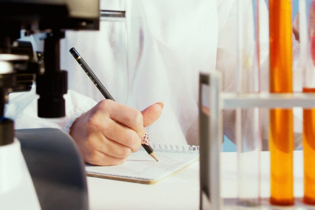 A person writing on a white notebook in a lab. Documentation Errors, how to avoid them in Pharma and Lab.